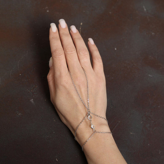 Silver chain bracelet connecting to a ring, adorned with bright sparkling white crystals, creating a stylish and elegant hand accessory
