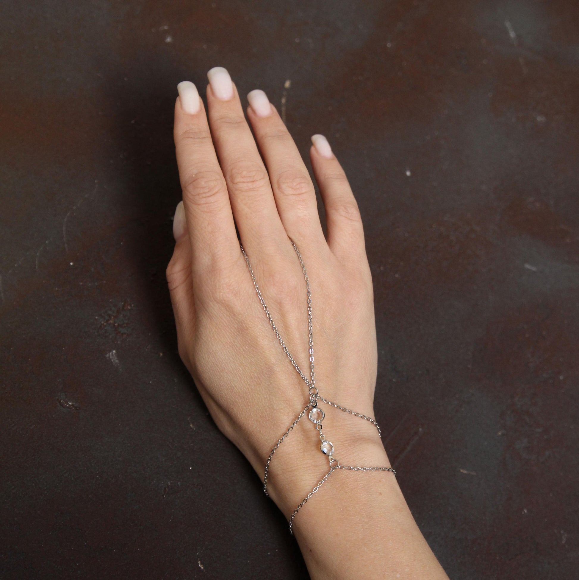 Silver chain bracelet connecting to a ring, adorned with bright sparkling white crystals, creating a stylish and elegant hand accessory