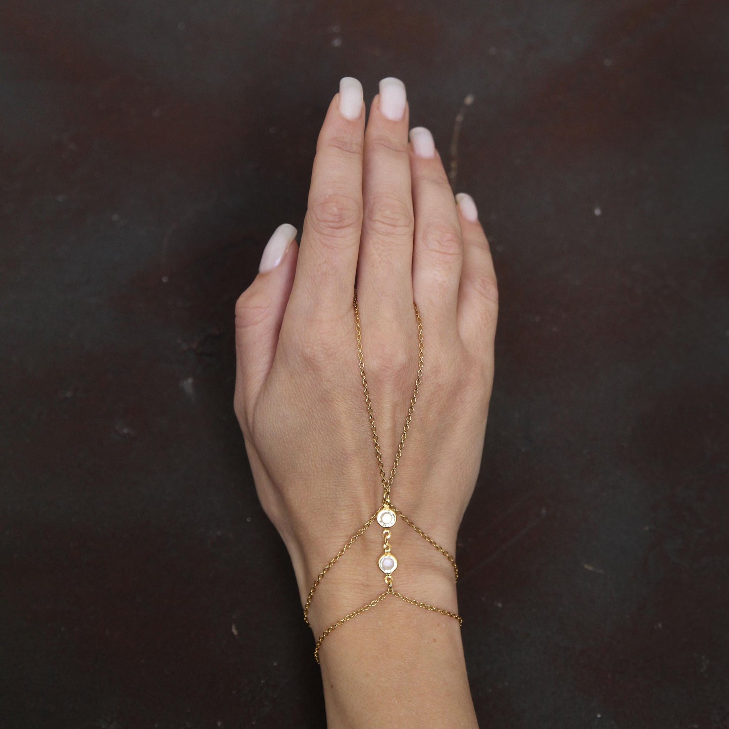 Gold chain bracelet connecting to a ring, adorned with bright sparkling white crystals, creating a stylish and elegant hand accessory